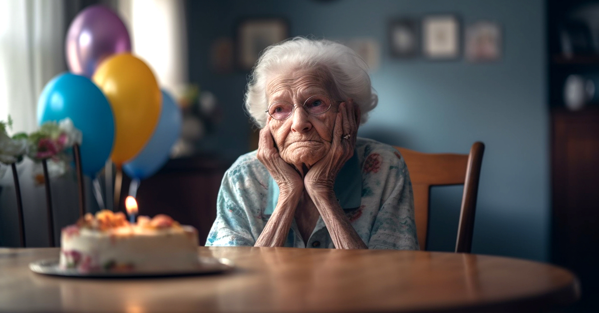Eine alte Dame sitzt traurig an einem Tisch. Vor ihr eine Geburtstagstorte und hinter ihr mehrere bunte Luftballons.