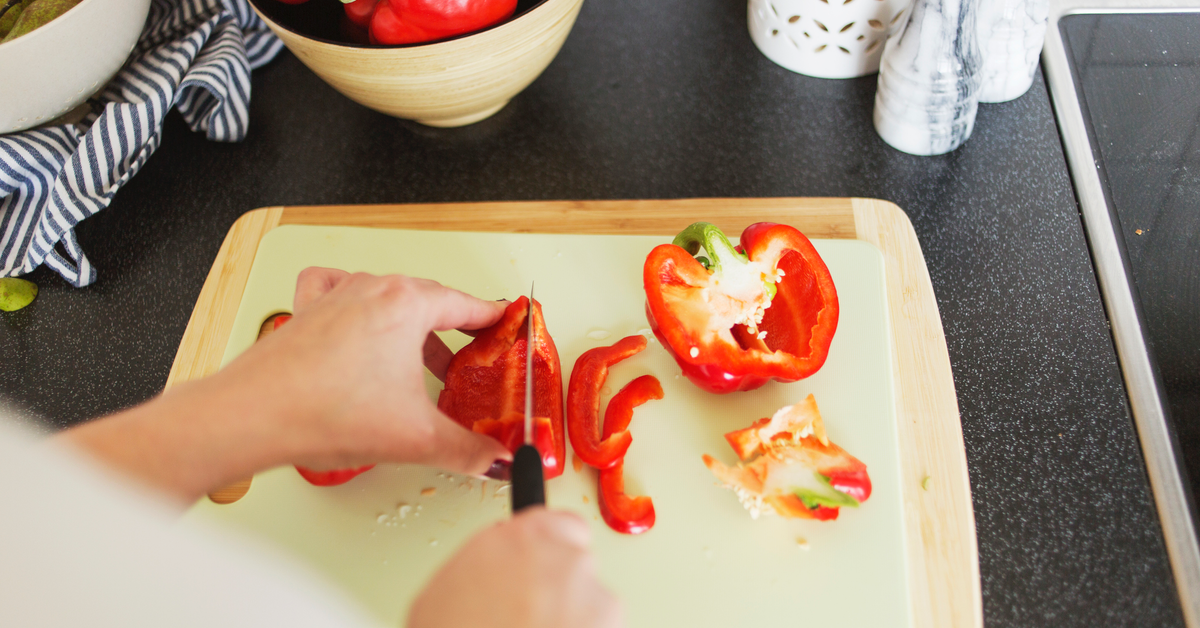 Man sieht, wie rote Paprika auf einem hellen Brett geschnitten werden.