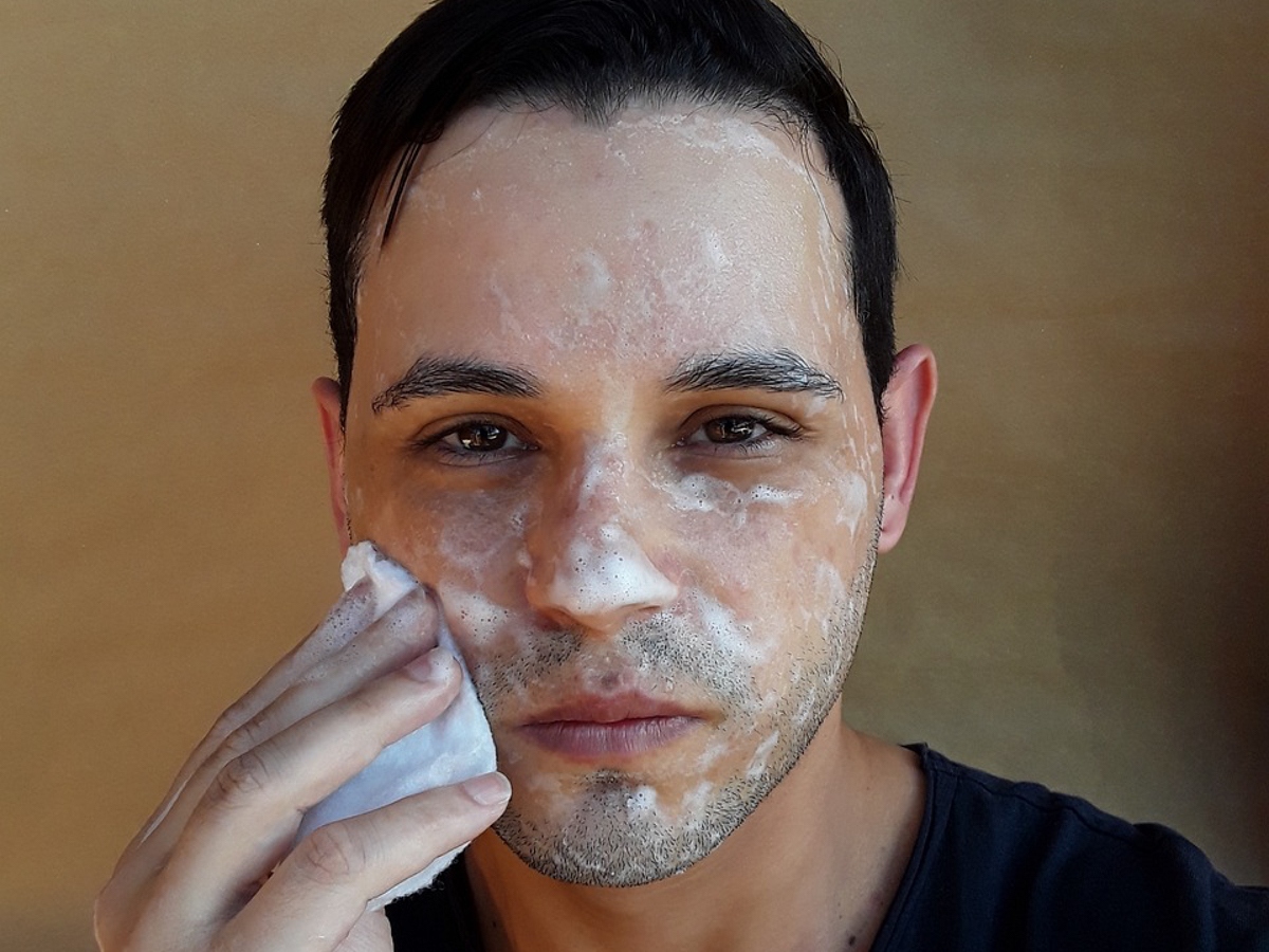Ein junger Mann wäscht sich mit Schaum sein Gesicht.