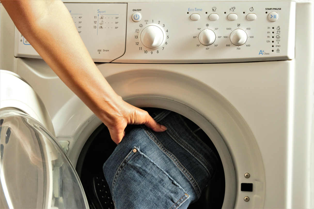 Jemand legt eine dunkelblaue Jeans in eine Waschmaschine, um sie zu waschen.