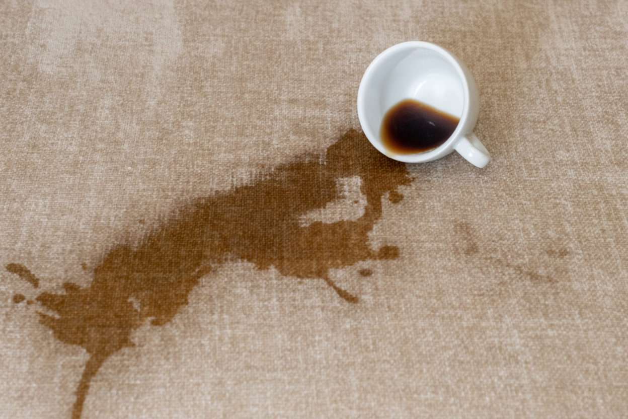 Eine Tasse Kaffee ist auf weichem Untergrund ausgekippt. Mit einem simplen Putztrick kannst du den Fleck entfernen.