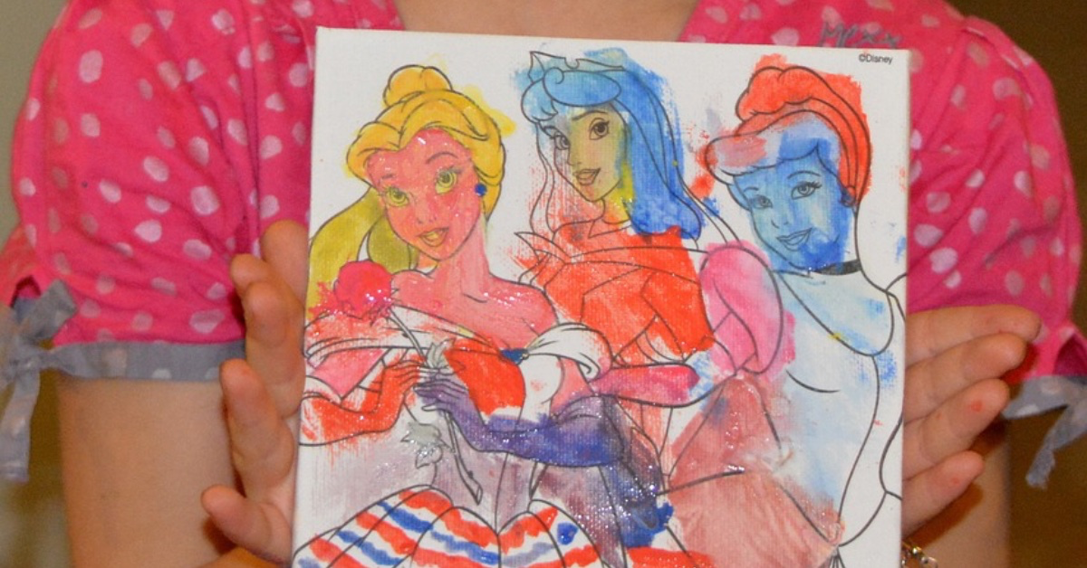 Mädchen zeigt stolz ein bunt ausgemaltes Bild mit drei Disney-Prinzessinnen. Allein spielen fördert Selbständigkeit und Selbstbewusstsein.
