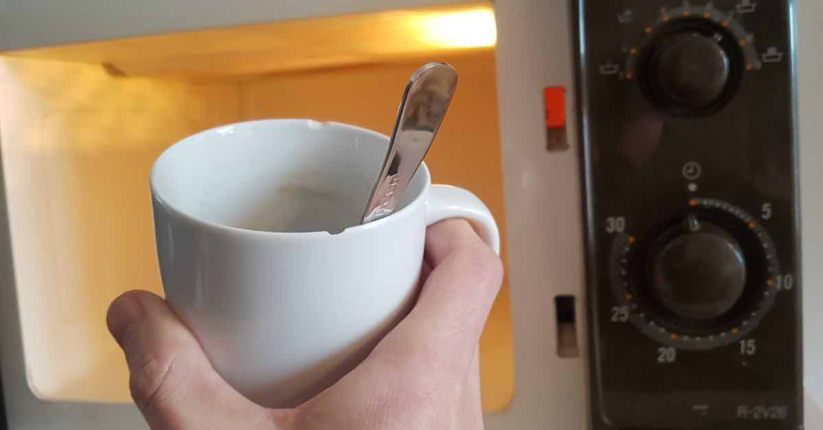 Hand stellt Tasse mit Metall-LÃ¶ffel in die Mikrowelle.