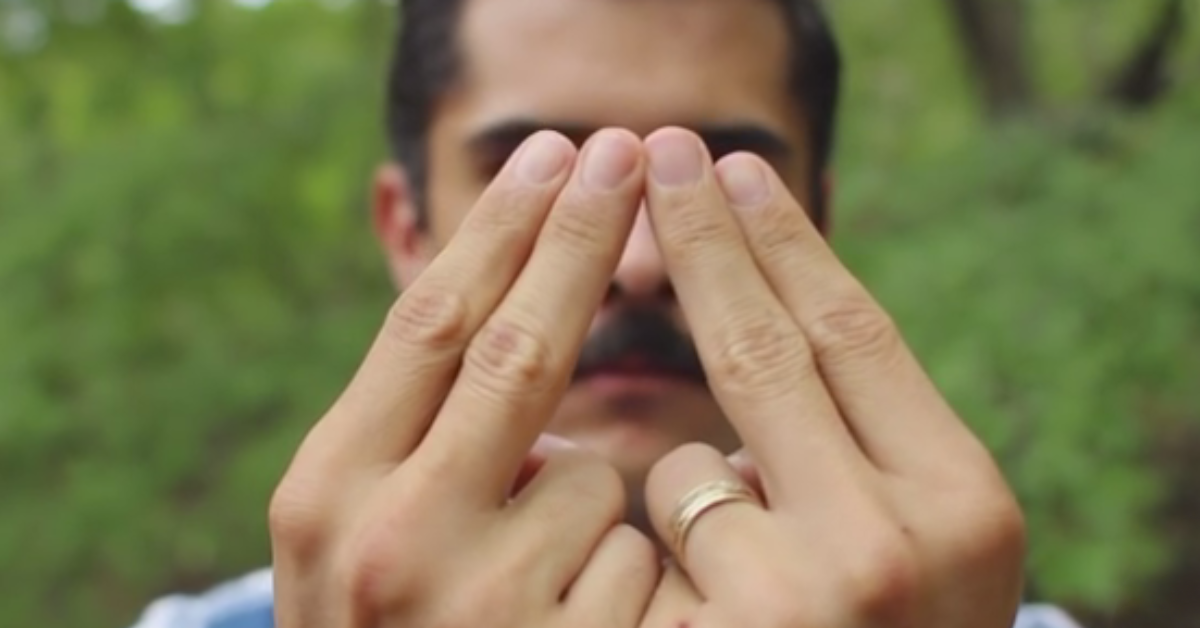 Mann hÃ¤lt Zeige- und Ringfinger der linken und rechten Hand zu einem Dreieck zusammen.