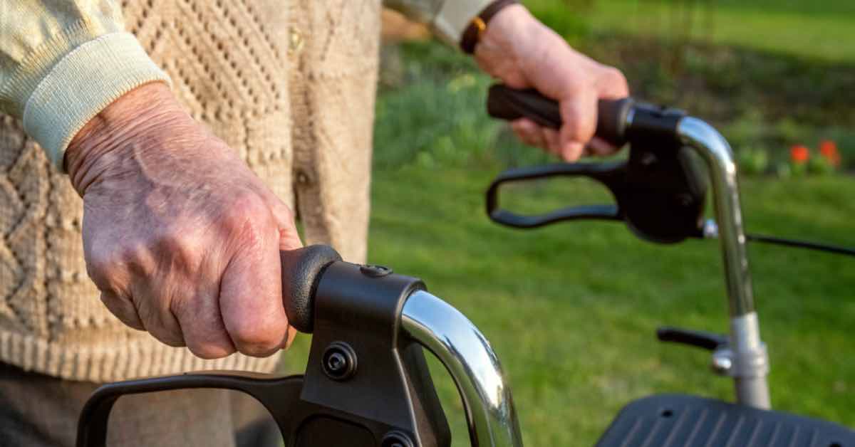 Frau geht mit Rollator durch den pflegeleichten Garten.