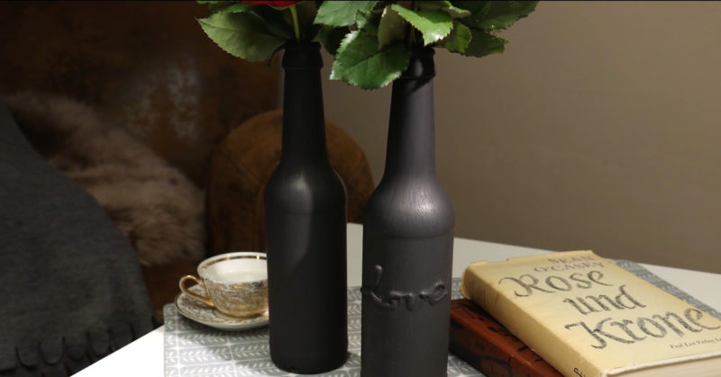 Zwei schwarze Vasen stehen auf einem kleinen Tisch. Darin kann man Rosenstiele erahnen.