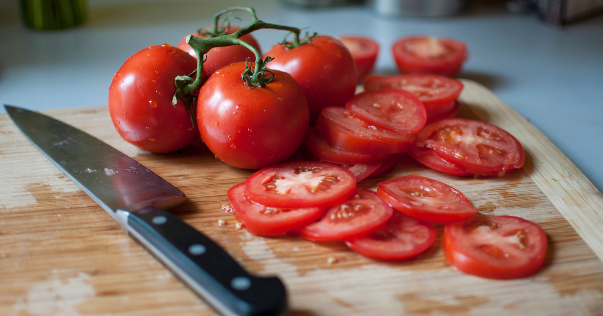 Tomaten auf einem Schneidebrett. Teils noch ganz, teils in Scheiben geschnitten. Daneben liegt ein Messer auf dem Brett