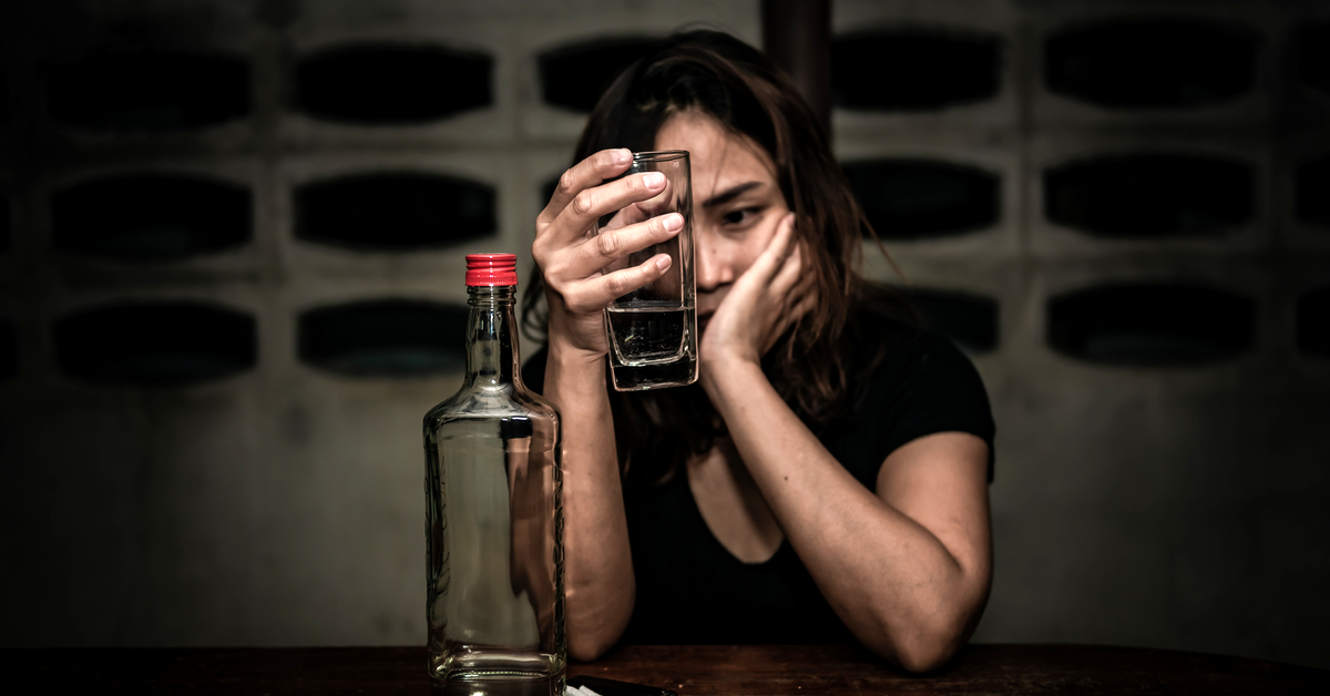 Eine Frau hÃ¤lt ein Glas in der Hand, vor ihr steht eine leere Flasche. Sie ist wahrscheinlich betrunken.