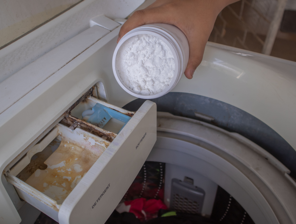 Jemand gibt Natron in das Waschmittelfach, um seine Waschmaschine zu reinigen.