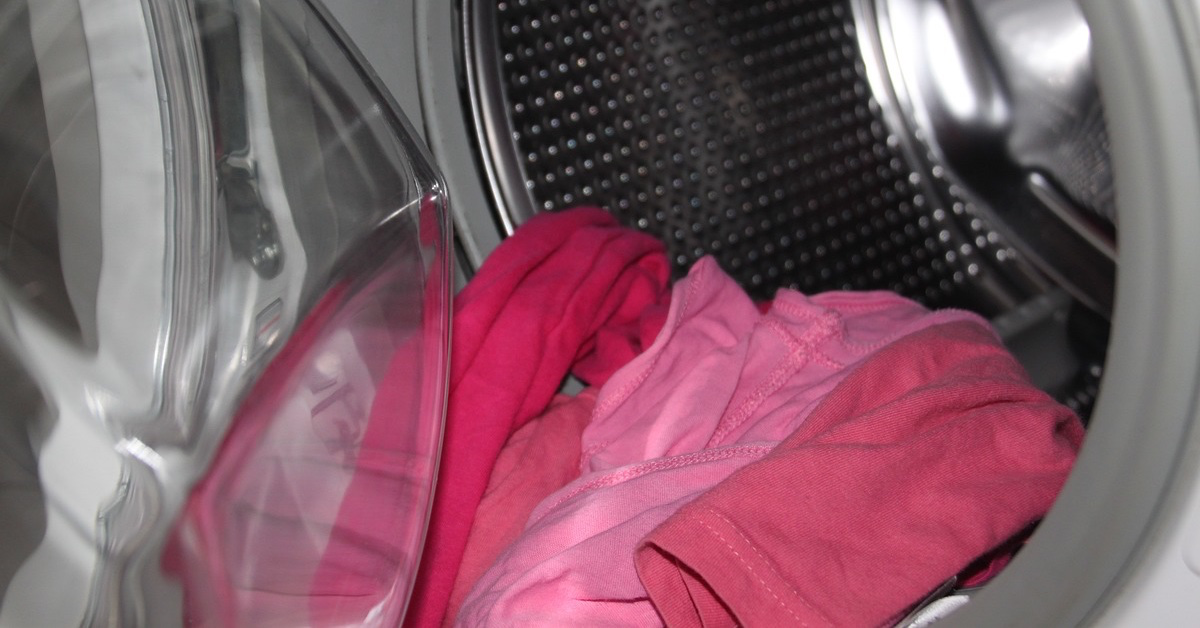 Rote Buntwäsche hängt aus einer geöffneten Waschtrommel heraus.