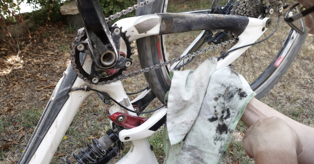 Ein Lappen voller Dreck und Schmiere, im Hintergrund ein schmutziges, weißes Fahrrad, das auf dem Kopf steht.