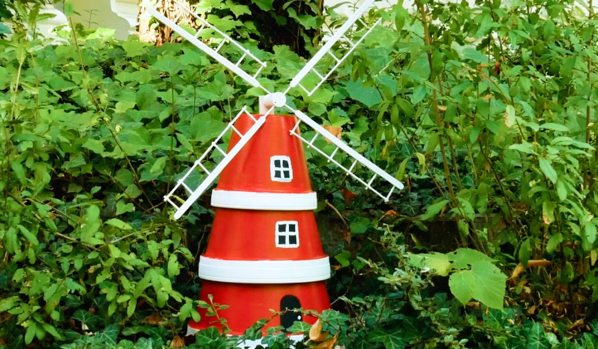 Eine aus Blumentöpfen gebastelte Windmühle als Garten-Deko steht in einem Vorgarten.