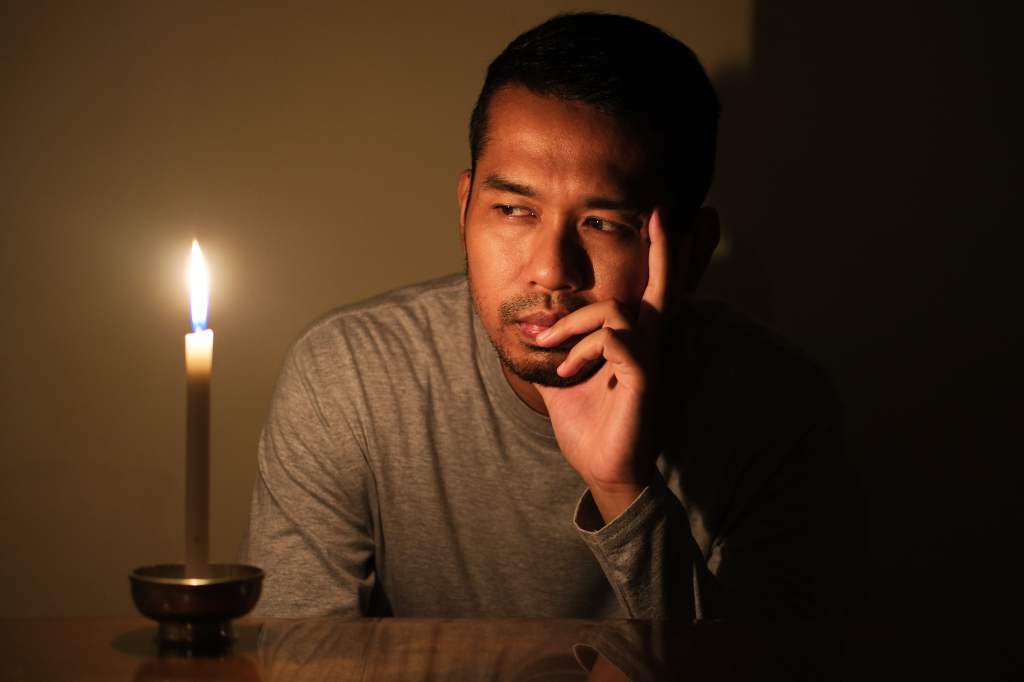 Mann sitzt im Dunkeln vor einer Kerze
