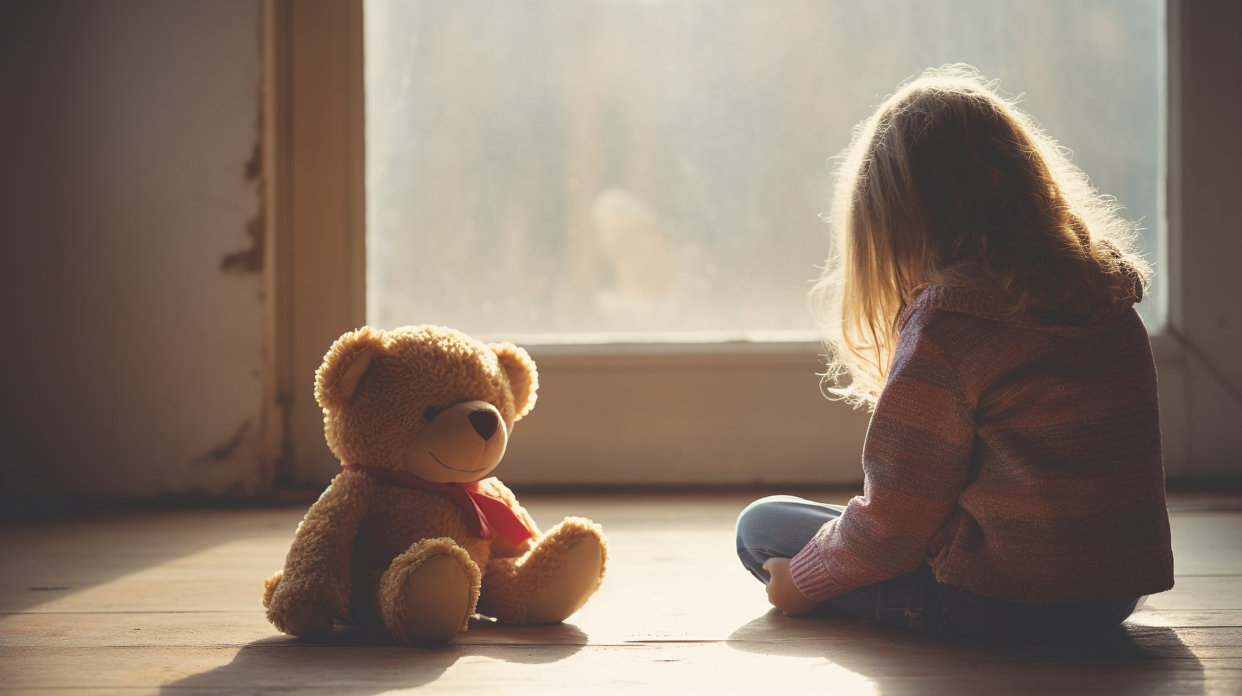 Kind sitzt einsam mit Teddy auf dem Boden