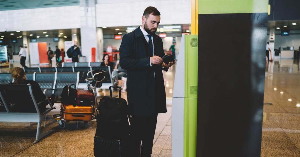 Mann steht an einem Automaten am Flughafen.