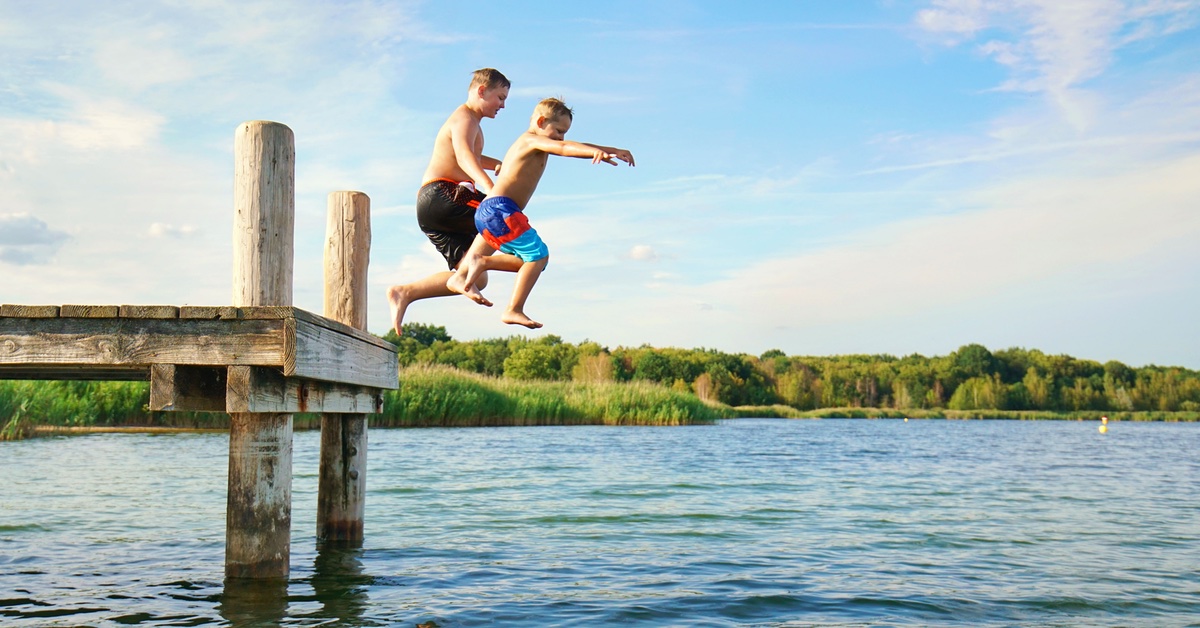 Kinder springen von einem Steg ins Wasser 