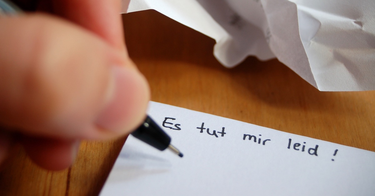 Eine Person schreibt "Es tut mir leid" auf einen Zettel 