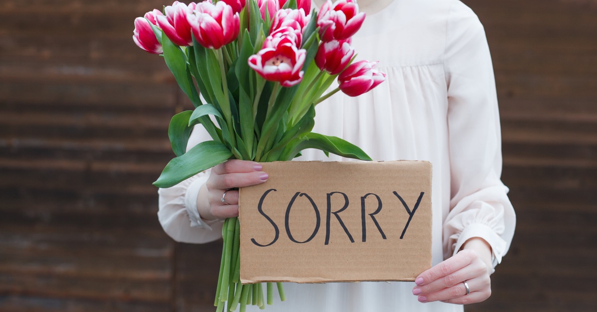 Eine Person hÃ¤lt Blumen und ein Schild mit "Sorry" in der Hand. 