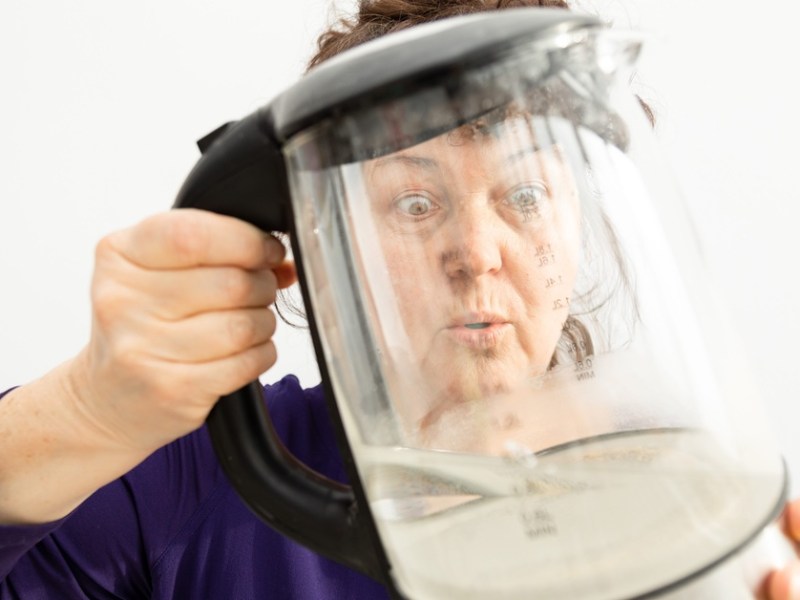 Frau guckt einen Wasserkocher ungläubig an.