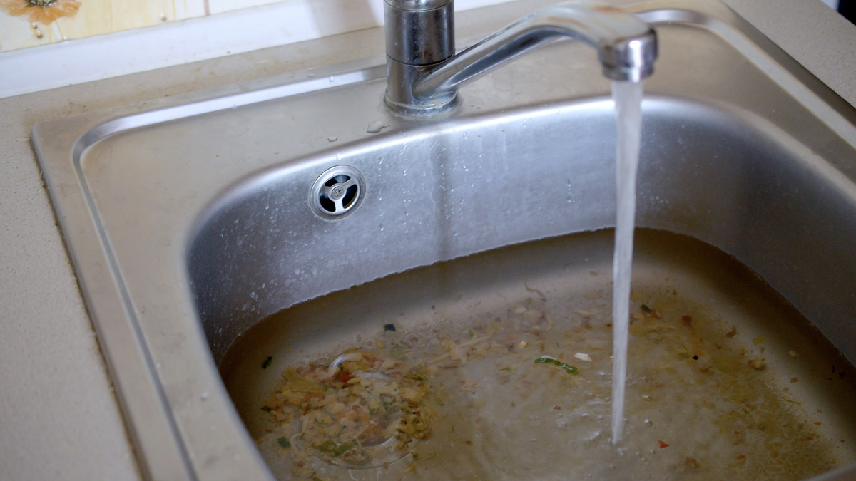 Ein schmutziges Waschbecken in einer Küche wird mit Wasser befüllt.