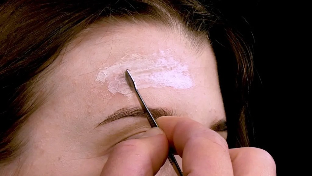 Mit Kleber und Zellstoff wird eine künstliche Narbe auf der Stirn modelliert. 