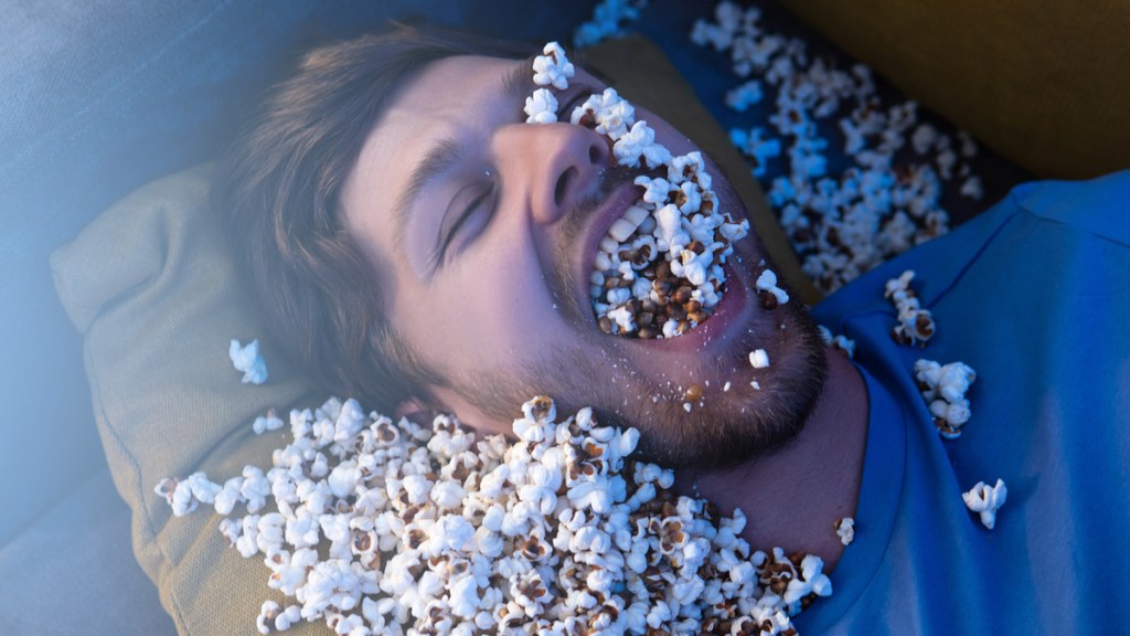 Ein Mann hat Popcorn im Gesicht und im Mund.