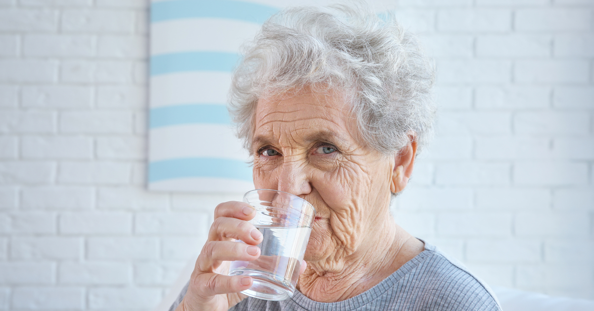 Eine Ã¤ltere Frau mit kurzen grauen Haaren trinkt Wasser aus einem Glas.