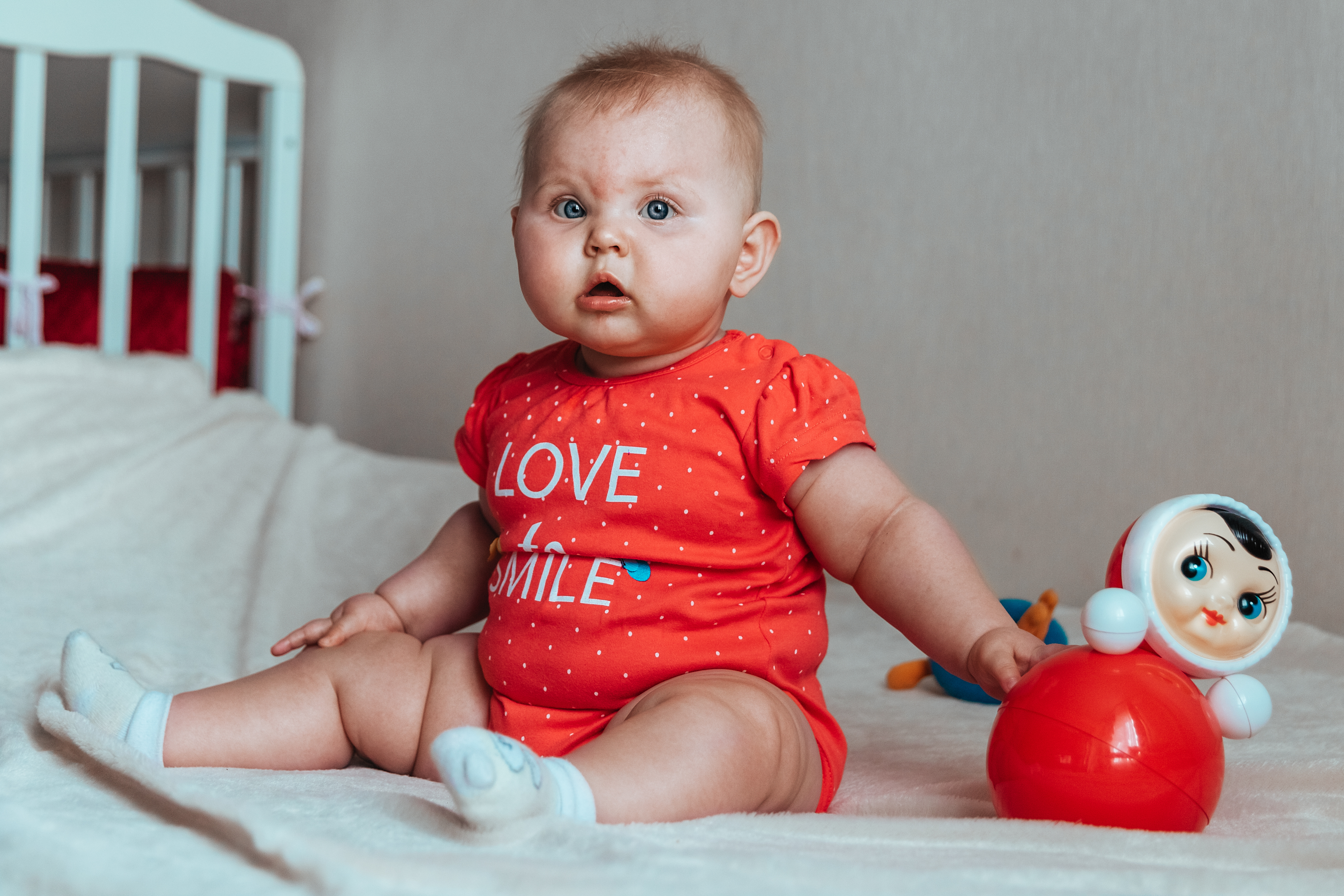 Ein Baby sitzt neben einem StehaufmÃ¤nnchen und blickt in die Kamera.