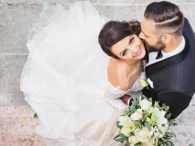 Ein Hochzeitspaar wird von oben fotografiert. Die Braut schaut glücklich nach oben in die Kamera.