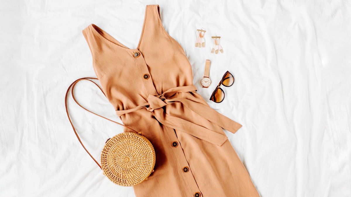 Braunes Kleid und Tasche liegen als Sommeroutfit auf einem weiÃŸen Bett