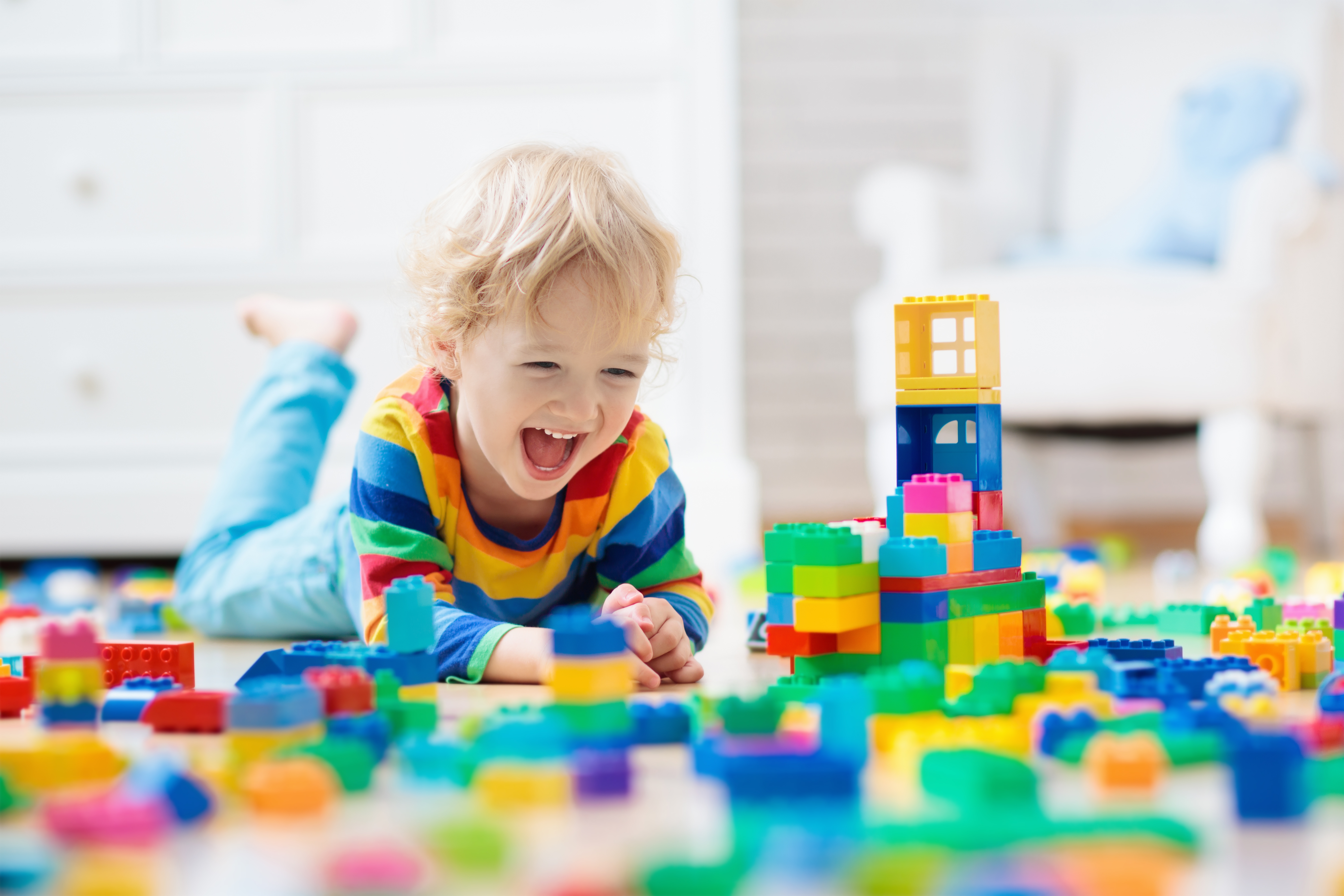 Ein Kind spielt mit bunten Duplo-Steinen und freut sich.