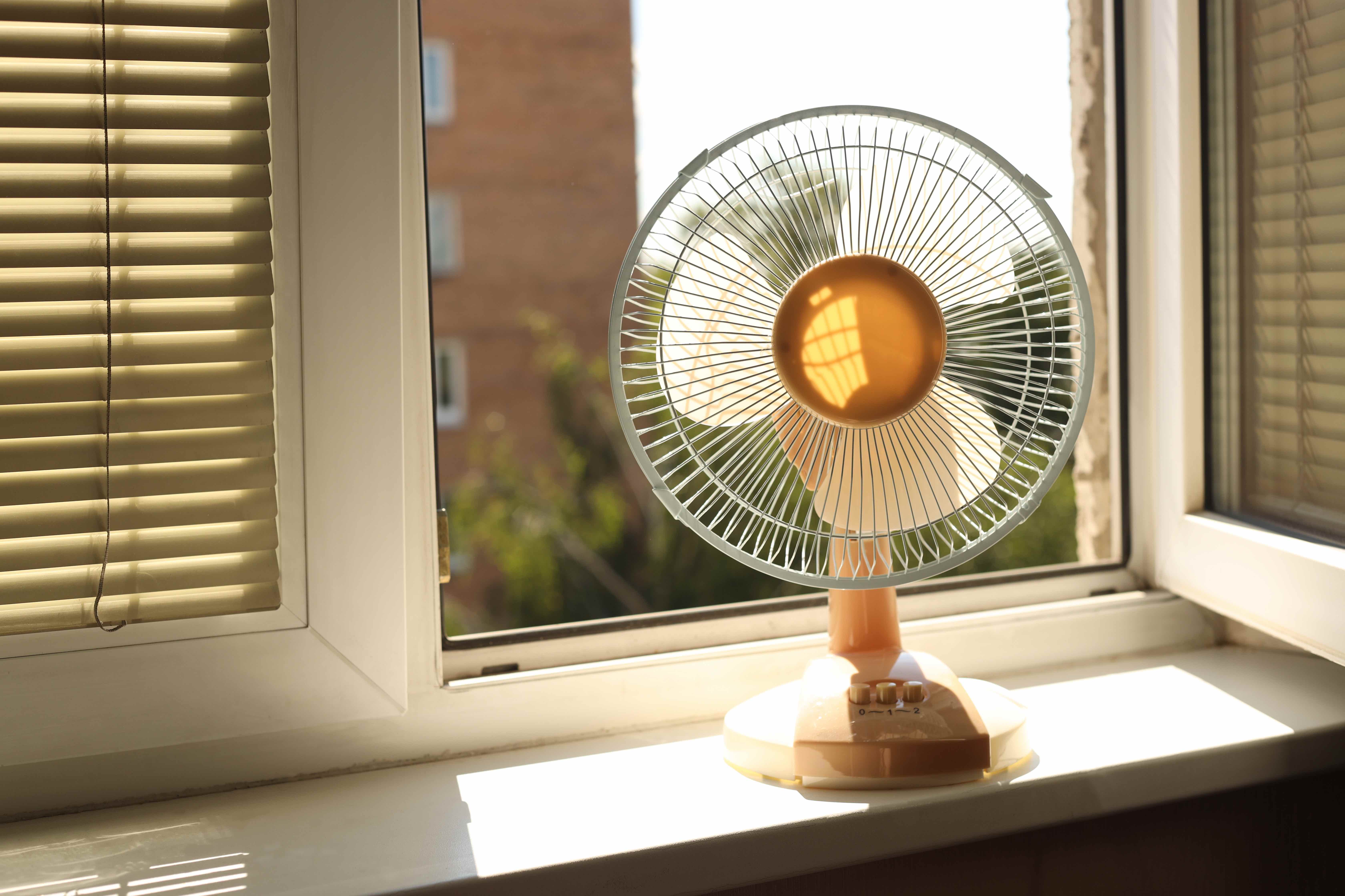 Ein Ventilator, der bei offenem Fenster auf einem Fensterbrett steht. Diese Tipps zeigen, wie man einen Ventilator richtig aufstellt.