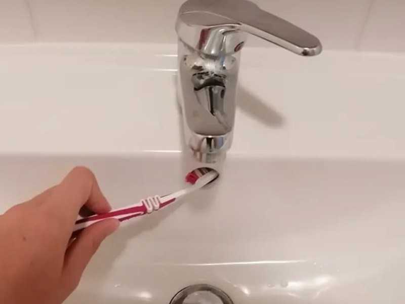 Waschbeckenüberlauf wird mit einer Zahnbürste gereinigt.