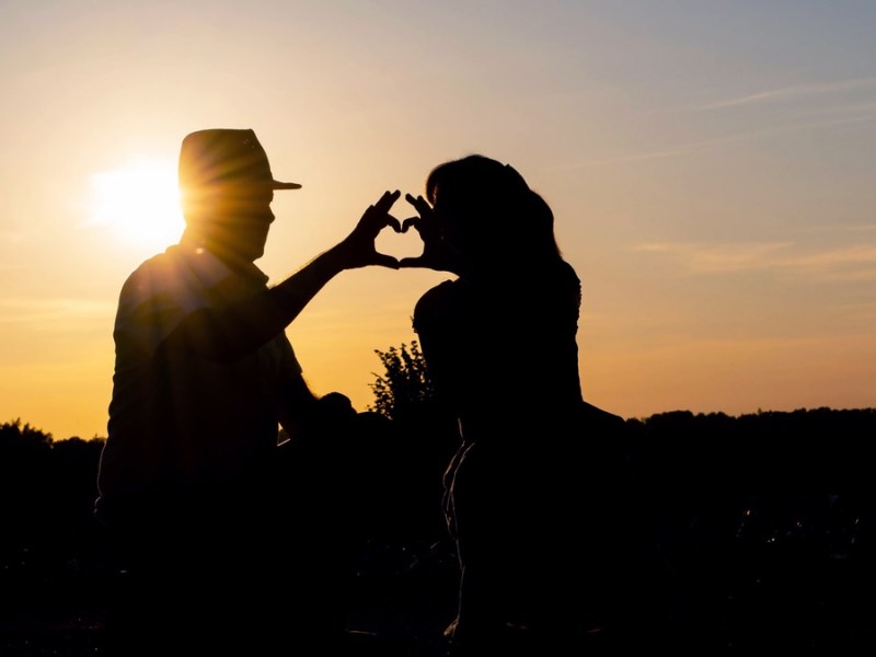 Paar formt bei Sonnenuntergang mit den Händen ein Herz.