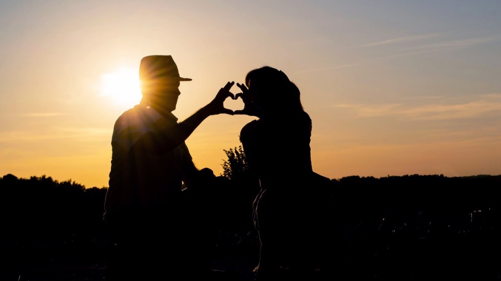 Paar formt bei Sonnenuntergang mit den Händen ein Herz.