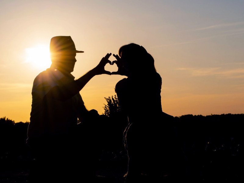 Paar formt bei Sonnenuntergang mit den Händen ein Herz.