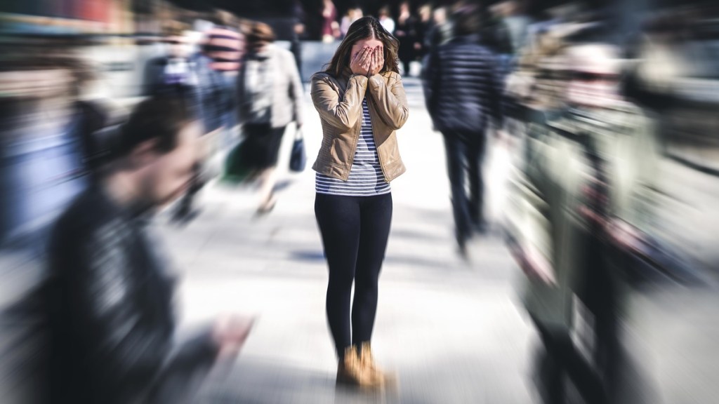 Frau steht in der Mitte von vielen Menschen und hält sich die Augen zu.