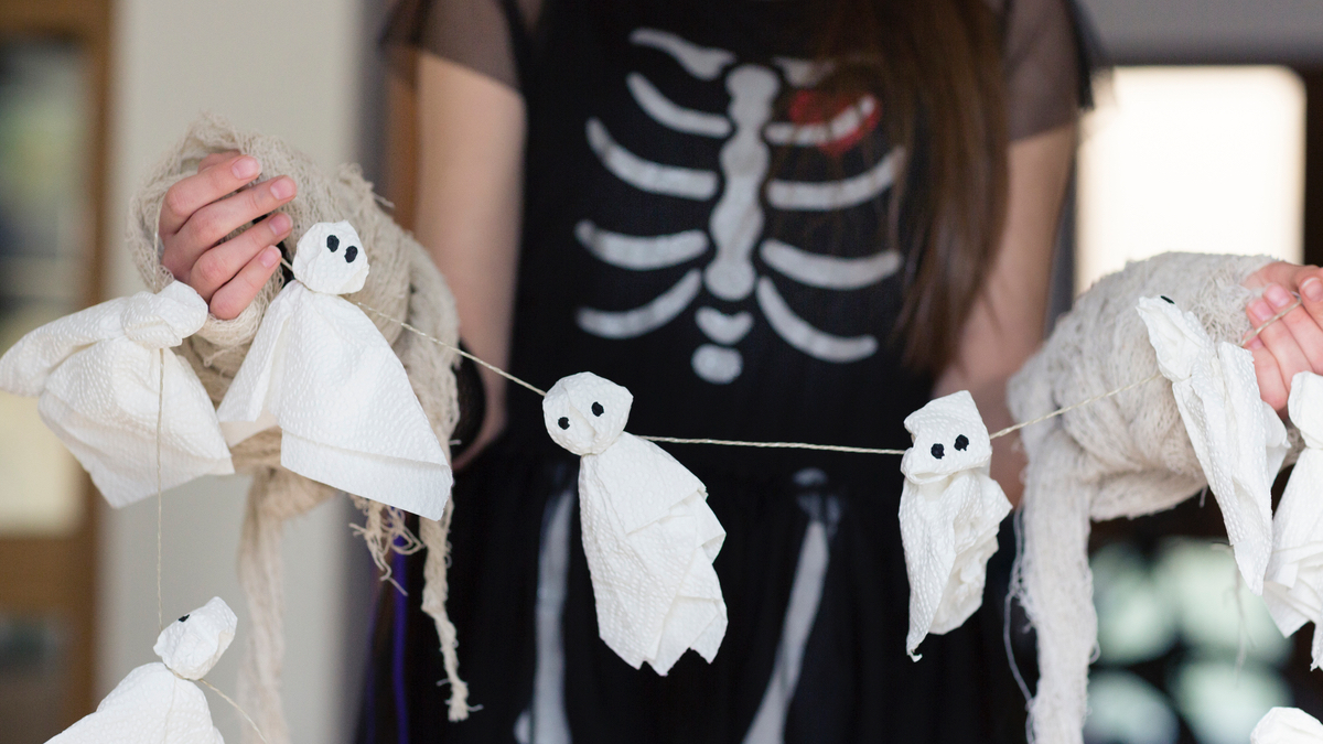Eine Frau in einem Skelettkostüm hängt eine Geister-Girlande auf.