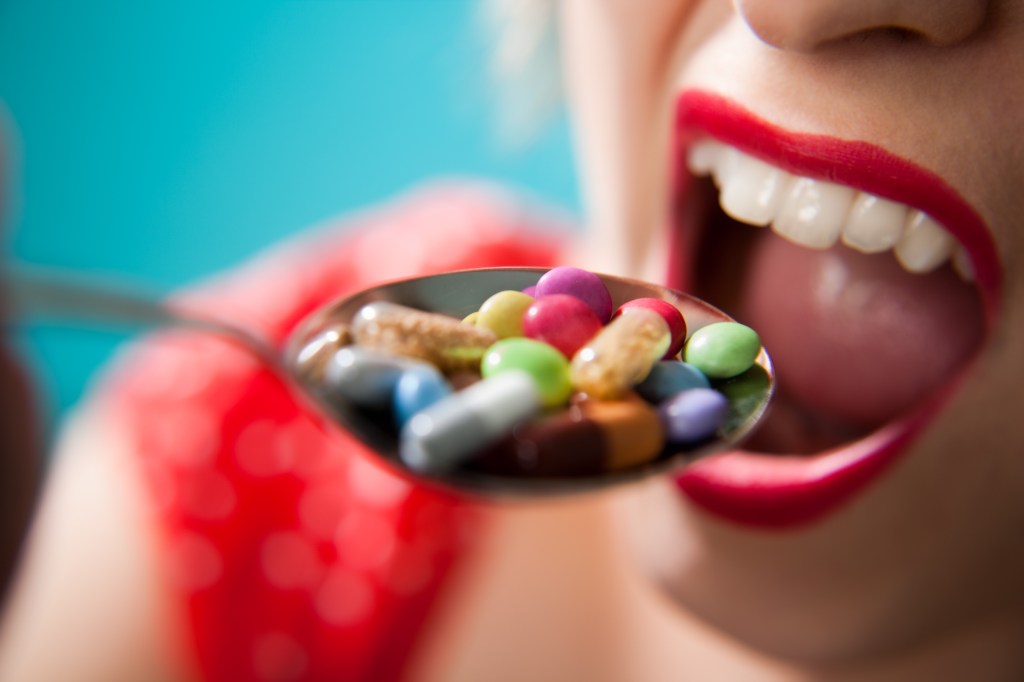 Eine Frau schiebt einen Löffel voller bunter Pillen in ihren Mund.