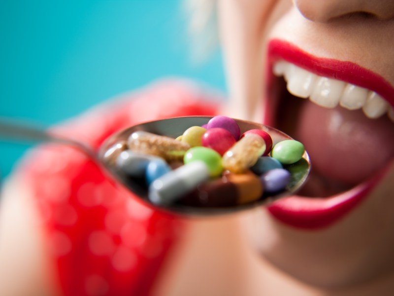 Eine Frau schiebt einen Löffel voller bunter Pillen in ihren Mund.