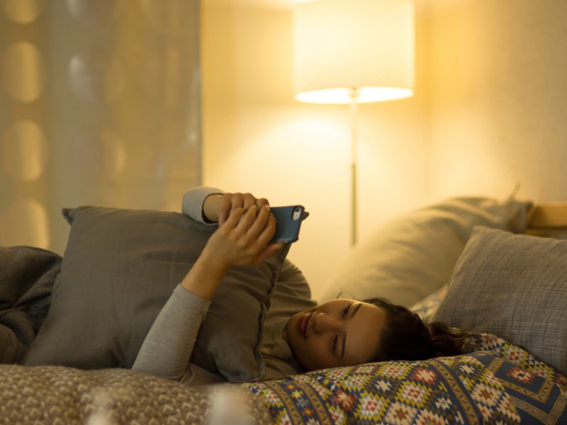 Eine Frau liegt auf dem Bett und schaut auf ihr Handy.