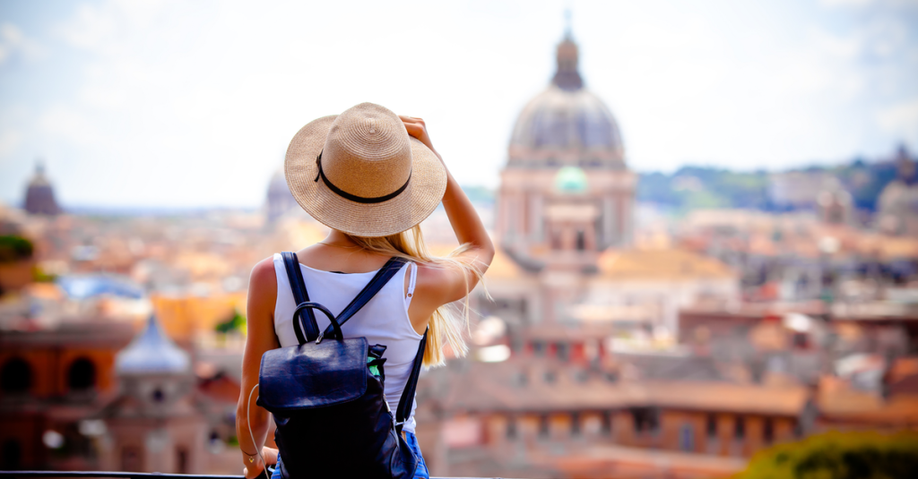 Eine Frau mit Hut und kurzer Kleidung steht mit dem Rücken zum Betrachter und schaut sich Rom an.
