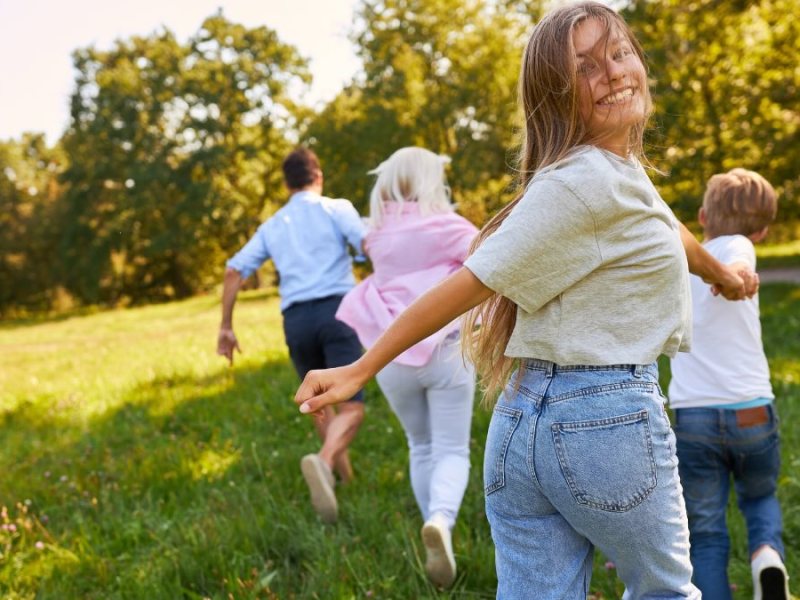 Eine Familie rennt fröhlich über eine Wiese. Das Mädchen hinten schaut glücklich in die Kamera.