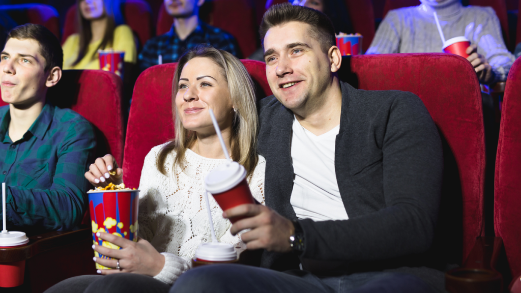 Ein Pärchen sitzt mit Popcorn und Getränken in einem Kinosaal.