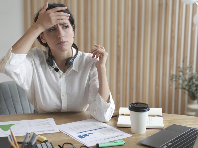 Eine Frau sitzt am Schreibtisch und greift sich an den Kopf, als habe sie Kopfschmerzen.
