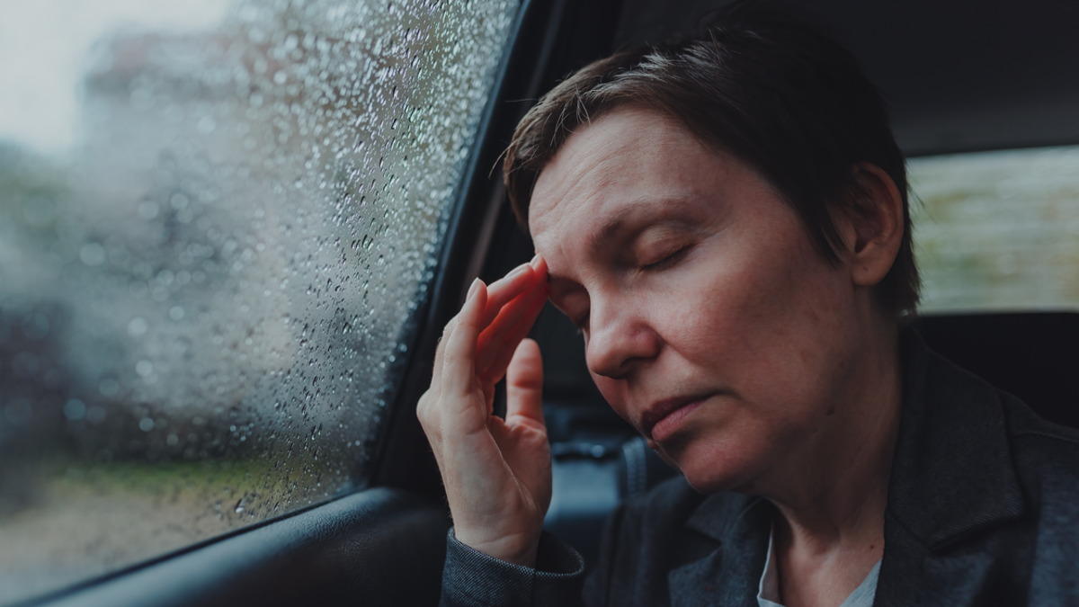 Eine Frau lehnt ihren Kopf an die Scheibe eines Autos und fest sich mit einer Hand an den Kopf.