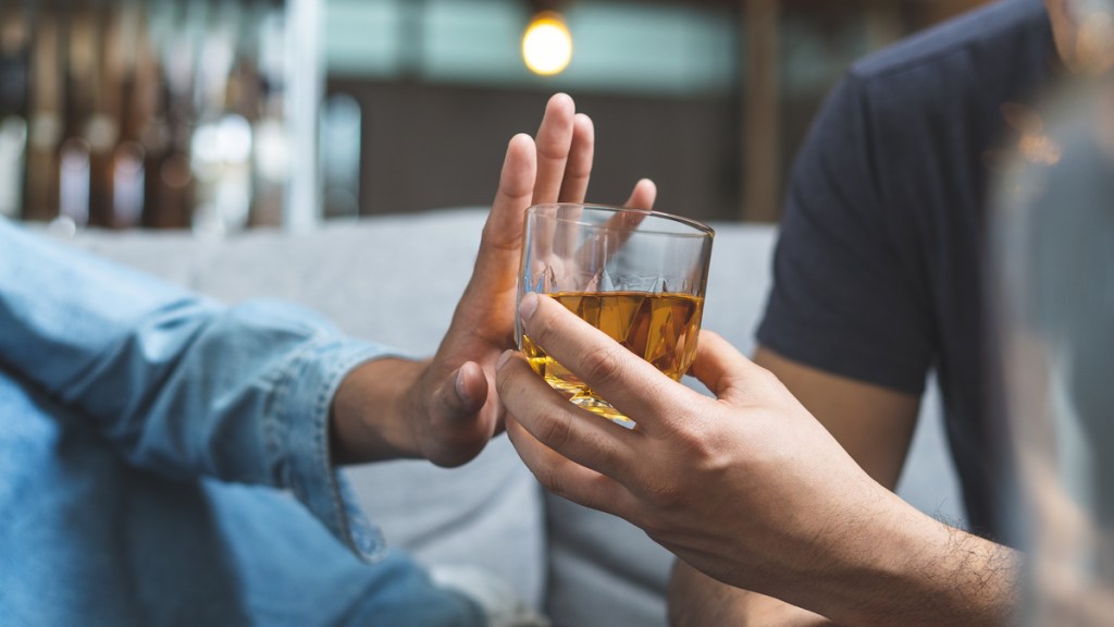 Eine Hand schiebt ein angebotenes Glas mit Alkohol von sich.