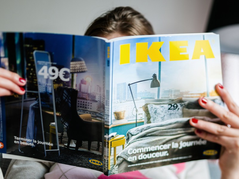 Eine Frau verbirgt ihr Gesicht hinter einem IKEA-Katalog.