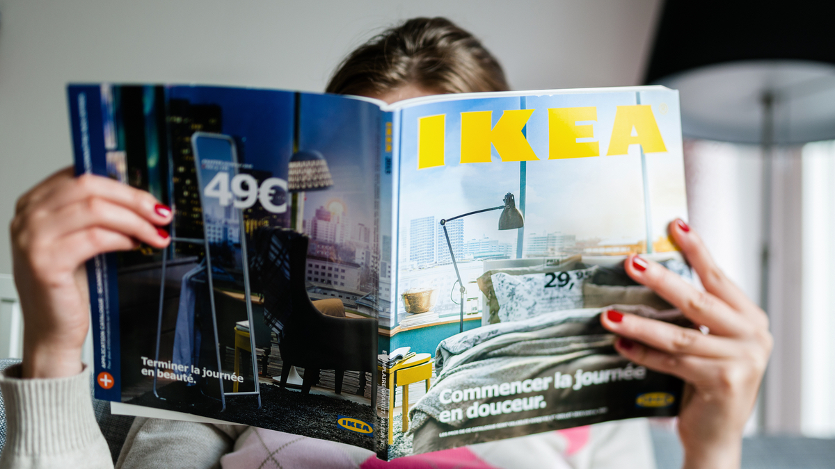 Eine Frau verbirgt ihr Gesicht hinter einem IKEA-Katalog.