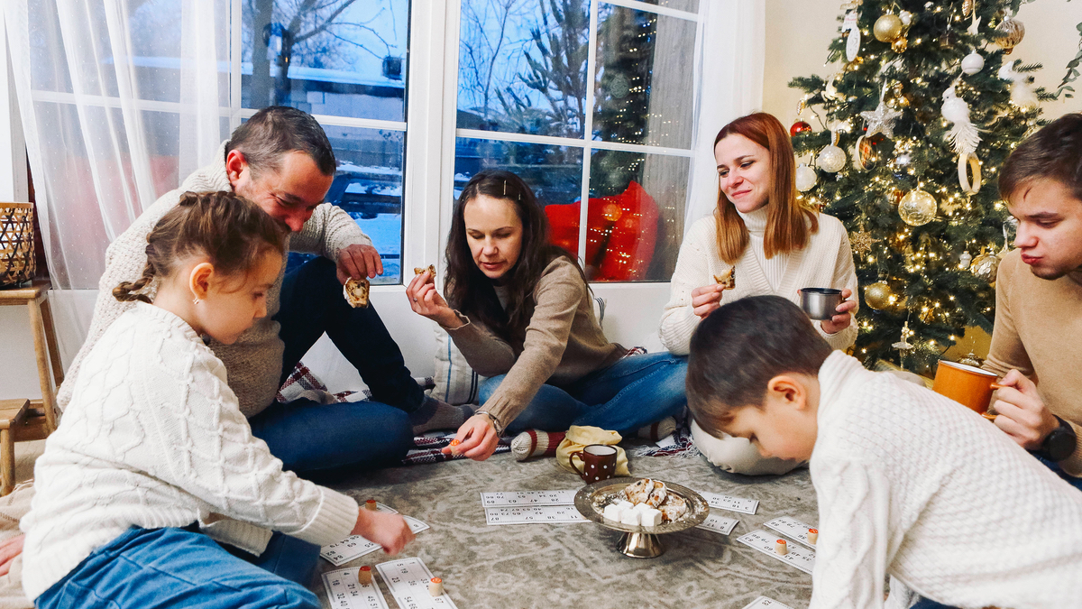Eine Familie sitzt auf dem Boden vor dem Weihnachtsbaum und spielt ein Gesellschaftsspiel.